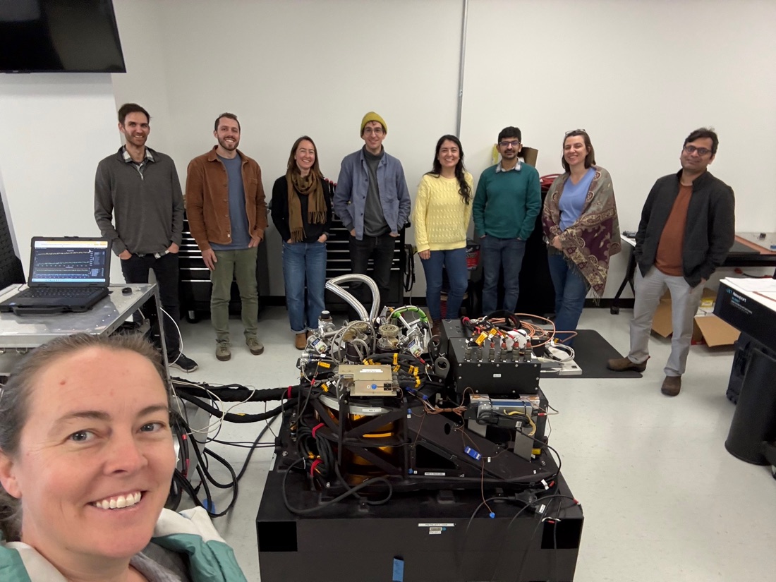 Members of the VSWIR-PLANTS team standing behind an imaging spectrometer on a lab bench.